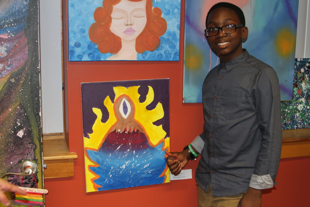 Youth member poses in front of his artwork
